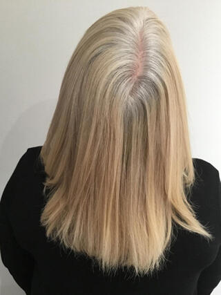 Foto "antes": vista trasera de una mujer con cabello rubio de longitud media con mechas negras antes de la coloración.